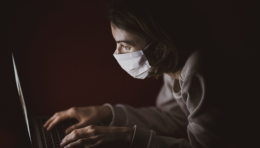 Woman in mask in the dark looking at computer screen